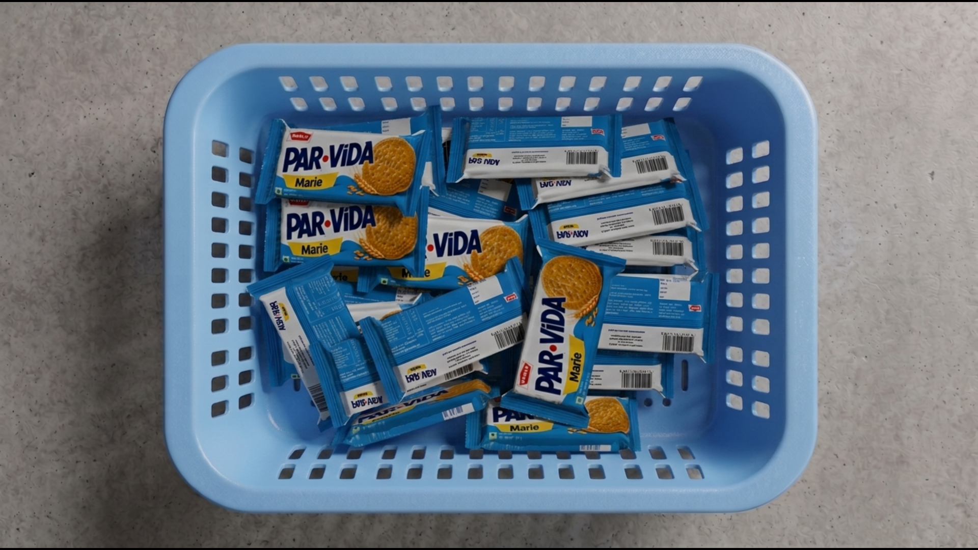 Top-down view of blue PAR-VIDA Marie biscuit sachets piled in a light blue ventilated plastic crate, with some packages showing front labels and others flipped to reveal barcode panels